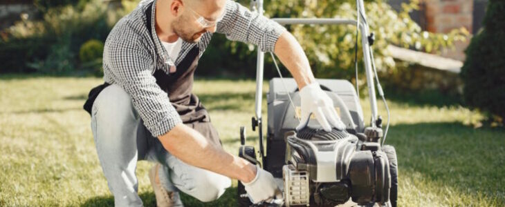 Man cutting grass with lawn mover in the back yard. Male in a black apron. Guy repairs.